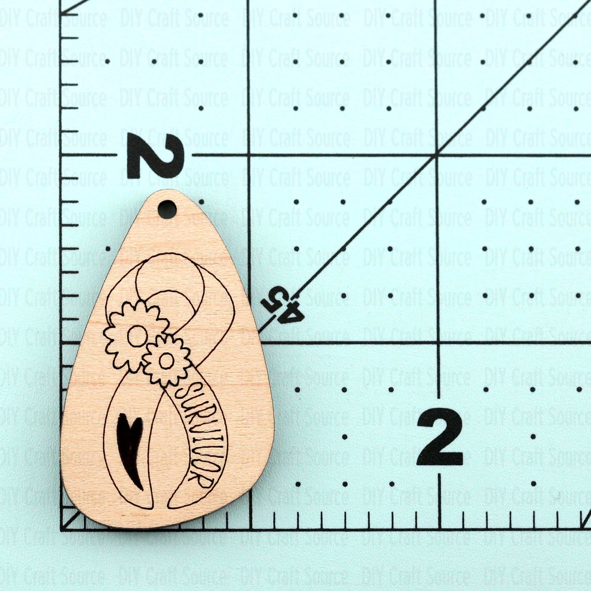 Wooden earring blanks with cancer survivor design on a light blue background with measurement scale.