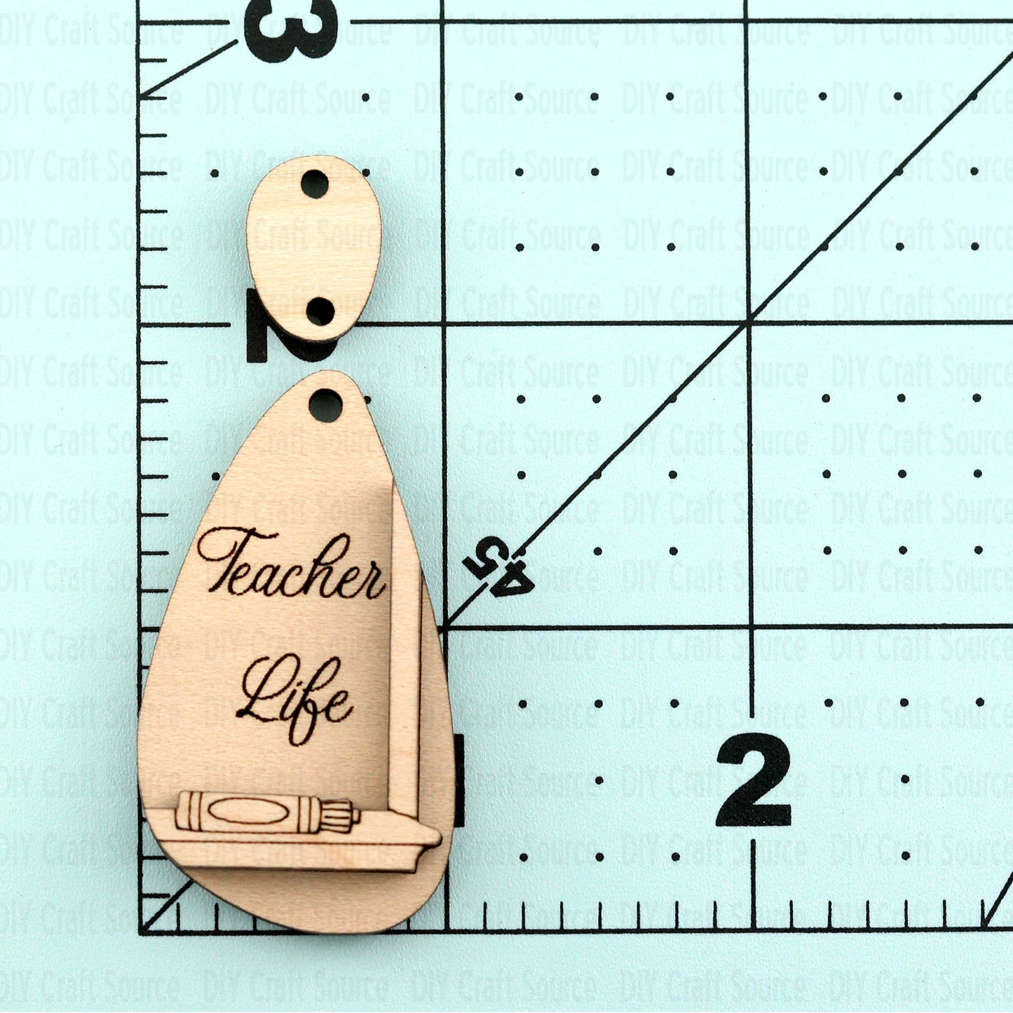 Wooden earring blank with 'Teacher Life' engraving on a ruler for scale