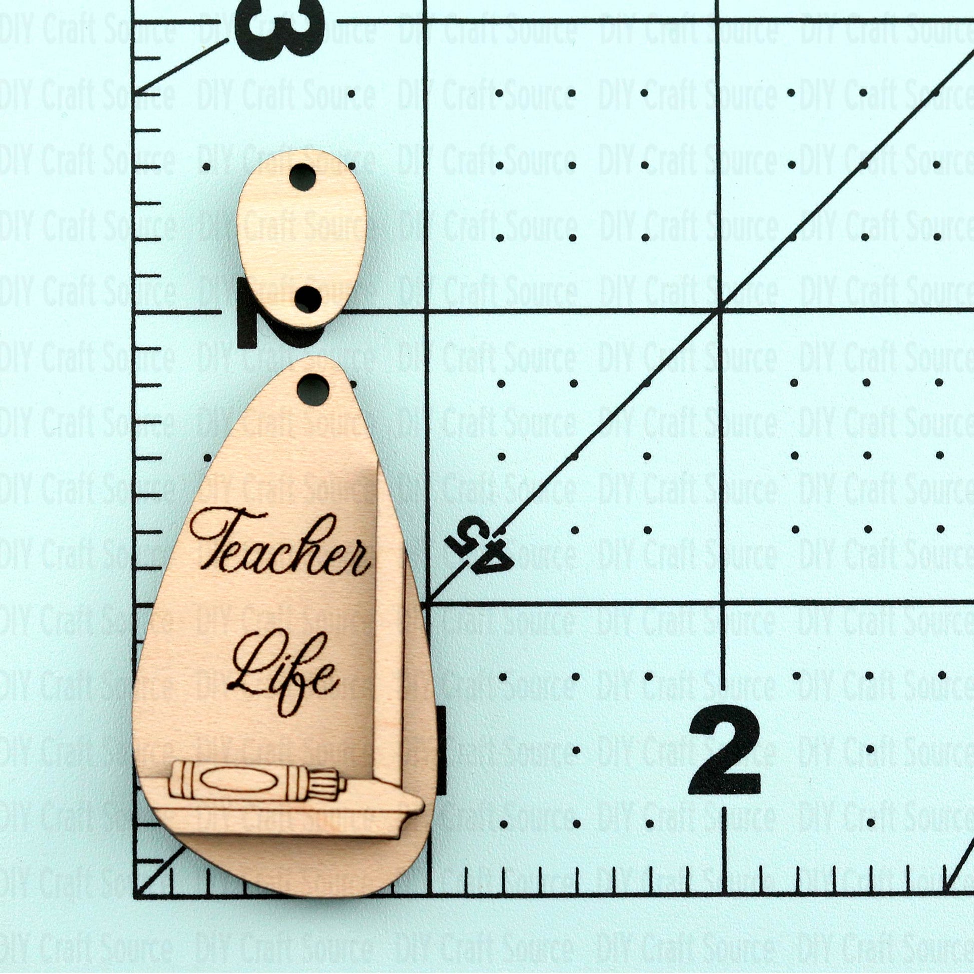 Wooden earring blank with 'Teacher Life' engraving on a ruler for scale